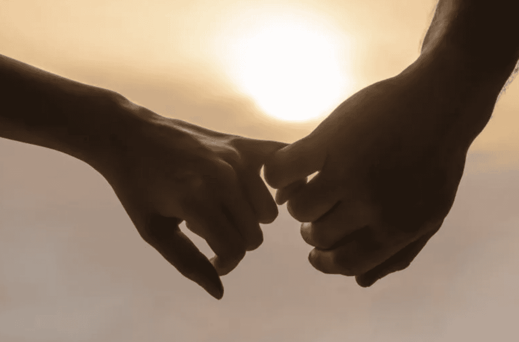 Two people holding pinkies with the sun setting in front of them